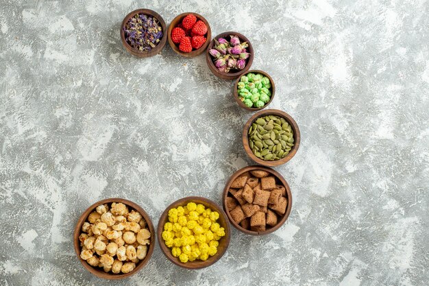 Vue de dessus différents bonbons avec des noix et des fleurs sur une surface blanche bonbons au thé gâteau au sucre beaucoup