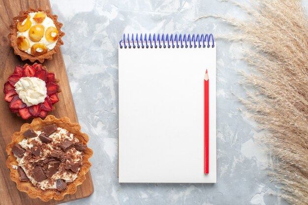 Vue de dessus différents gâteaux crémeux au chocolat et fruits bloc-notes sur le gâteau de bureau blanc cuire au four biscuit sucre sucré