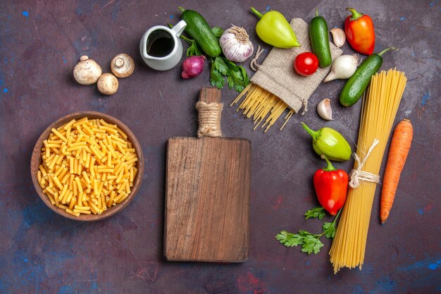 Vue de dessus différents ingrédients pâtes crues et légumes frais sur un bureau sombre produit repas frais salade santé régime