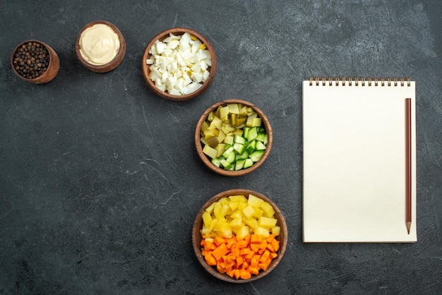 Vue de dessus différents ingrédients de la salade avec bloc-notes sur la surface grise collation repas légume salade