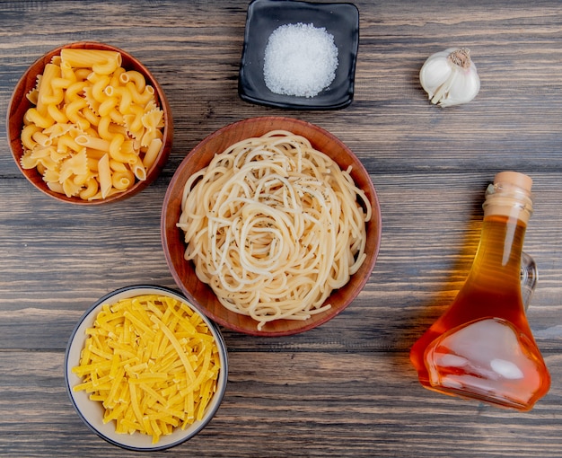 Vue de dessus de différents macaronis comme spaghetti tagliatelles et autres avec du beurre fondu à l'ail sel sur bois