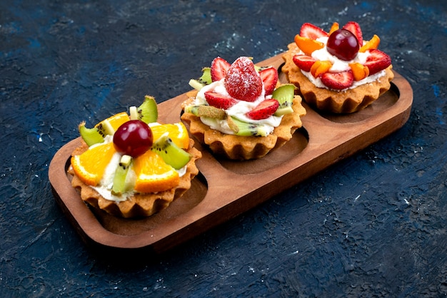 Une vue de dessus différents petits gâteaux avec de la crème et des fruits frais en tranches sur le fond bleu sucre gâteau aux fruits