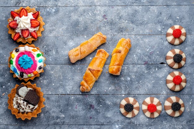 Vue de dessus de différents petits gâteaux avec des fruits tranchés bonbons bracelets au chocolat et baies sur gris, biscuit biscuit sucre sucré cuire