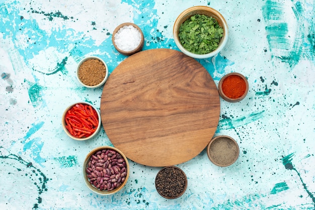 Photo gratuite vue de dessus de différents seasonigns avec poivrons haricots et verts sur un bureau bleu clair, ingrédient poivre épicé chaud