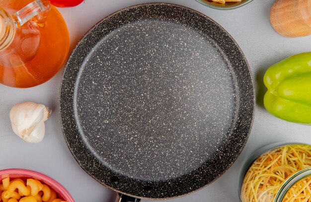 Vue de dessus de différents types de macaronis comme cavatappi et autres avec du beurre de tomate à l'ail poivron autour de la casserole sur violet