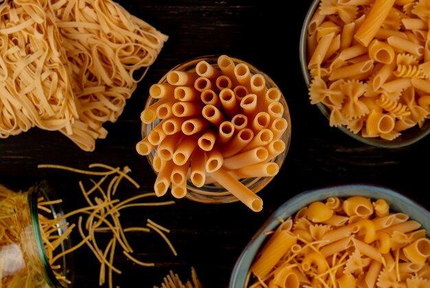 Vue de dessus de différents types de pâtes comme tagliatelles de spaghetti bucatini et autres sur la surface en bois