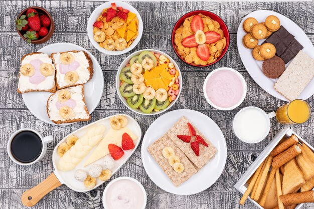 Vue de dessus de différents types de petit-déjeuner comme des toasts, des cornflakes, du yaourt et des fruits