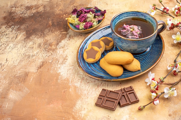 Vue de dessus de divers biscuits une tasse de thé et de fleurs de barres de chocolat sur table de couleurs mélangées