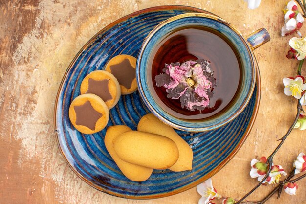 Vue de dessus de divers biscuits une tasse de thé et de fleurs sur table de couleurs mixtes