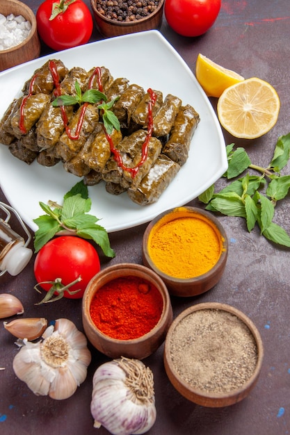 Photo gratuite vue de dessus dolma de feuilles délicieuses avec assaisonnements et tomates sur fond sombre plat laisse le dîner de viande de nourriture