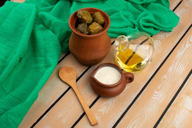 Vue de dessus dolma à l'intérieur du pot brun avec de l'huile d'olive et du yaourt sur le plancher rustique en bois