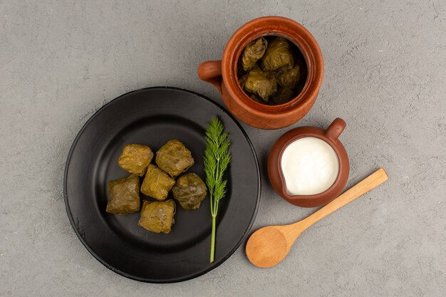 Vue de dessus dolma vert célèbre viande orientale avec de la viande hachée à l'intérieur de la plaque noire avec du yaourt sur le bureau gris