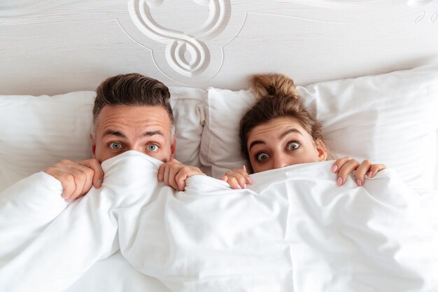 Vue de dessus du beau couple choqué couché ensemble dans son lit