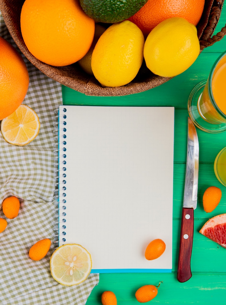 Photo gratuit vue de dessus du bloc-notes avec un couteau à kumquat au citron orange et du jus sur fond vert avec copie espace