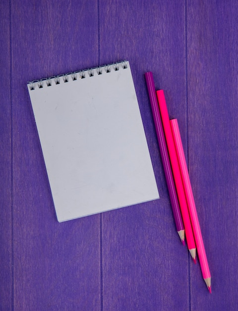 Vue de dessus du bloc-notes et des crayons de couleur sur fond violet avec espace copie
