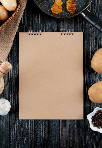 Photo gratuite vue de dessus du bloc-notes avec des croustilles de légumes poivre noir autour sur fond de bois avec copie espace