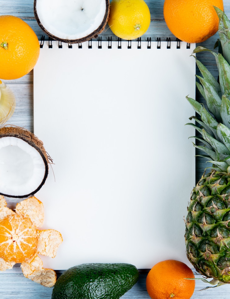 Photo gratuit vue de dessus du bloc-notes avec orange noix de coco mandarine avocat citron ananas autour sur fond de bois avec copie espace