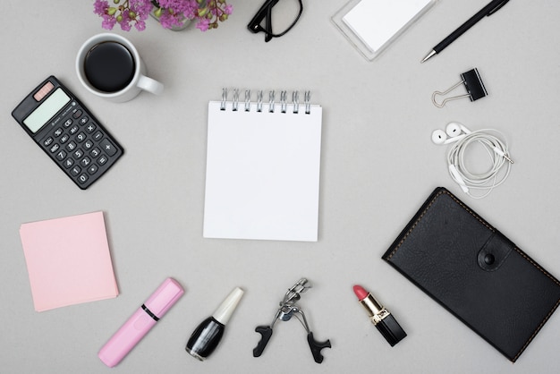 Vue de dessus du bloc-notes vide entouré d&#39;une tasse à café; calculatrice; objets de maquillage et écouteurs sur fond gris