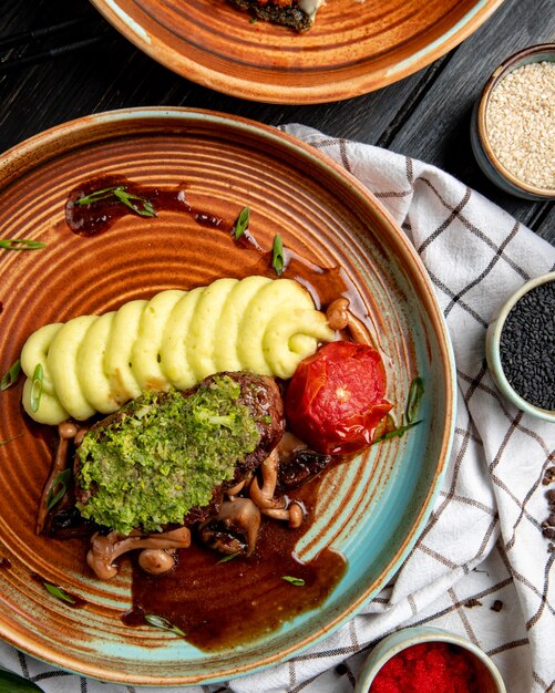 Vue de dessus du boeuf grillé avec purée de pommes de terre tomates champignons et sauce avocat dans une assiette sur bois