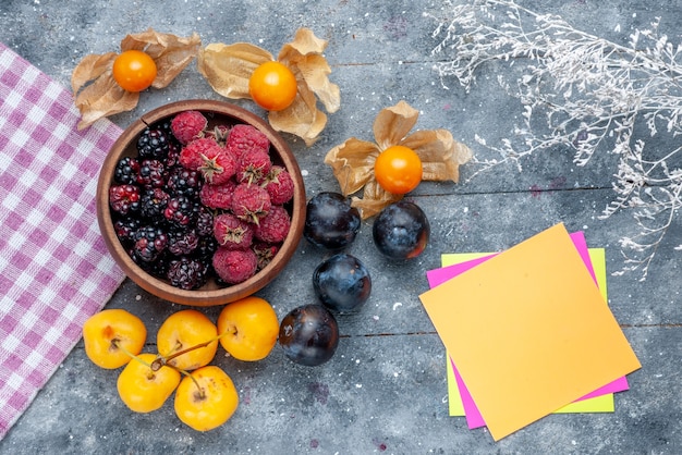 Vue de dessus du bol avec des baies fruits mûrs frais avec des cerises jaunes et des prunes sur gris rustique, berry fruit frais moelleux forêt