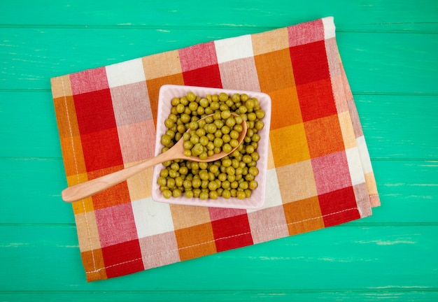 Vue de dessus du bol de pois verts avec une cuillère en bois sur un tissu et une surface verte