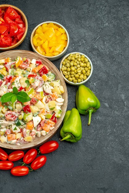 Vue de dessus du bol de salade de légumes avec des légumes sur le côté sur fond gris foncé