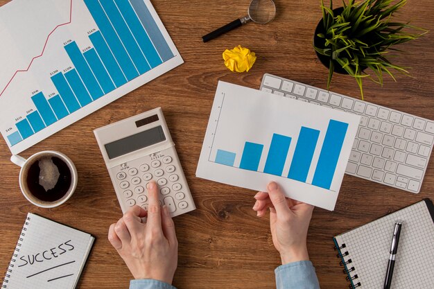 Vue de dessus du bureau avec courbe de croissance et mains à l'aide de minuscules calculatrices