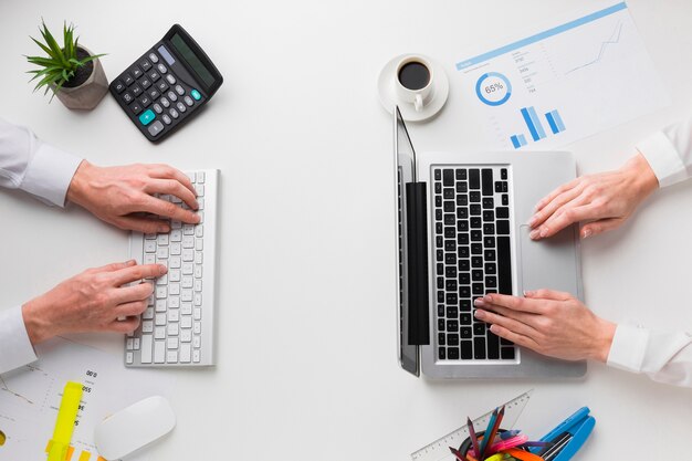 Vue de dessus du bureau avec les mains travaillant sur ordinateur portable et clavier