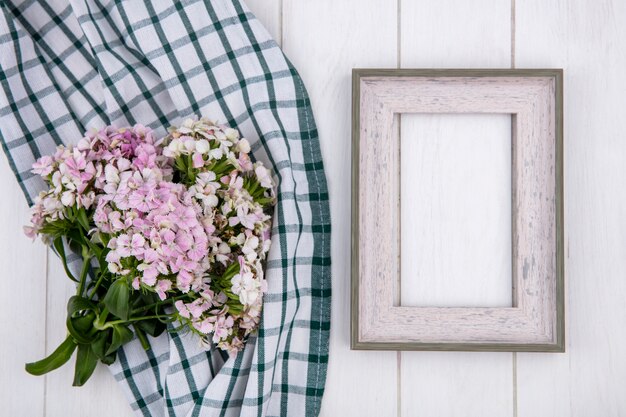 Vue de dessus du cadre blanc avec un bouquet de fleurs sur une serviette verte à carreaux sur une surface blanche