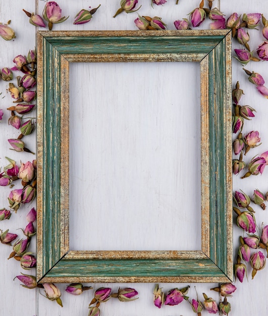 Vue de dessus du cadre or verdâtre avec des boutons de rose pourpres séchées sur une surface blanche