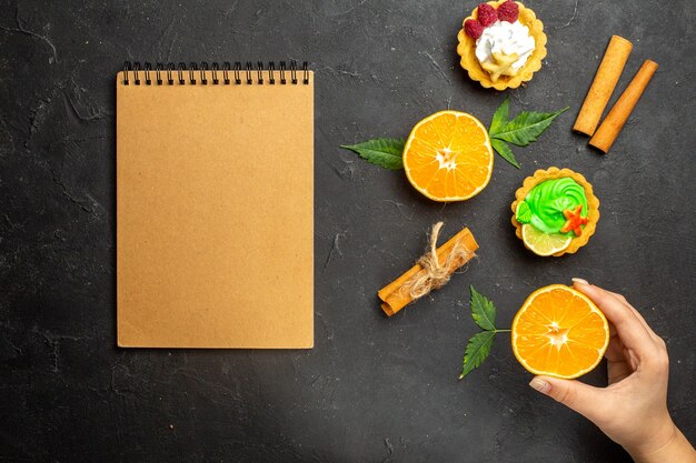 Vue de dessus du cahier de délicieux biscuits citrons verts à la cannelle et oranges à moitié coupées avec des feuilles sur fond sombre