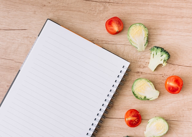 Une Vue De Dessus Du Cahier à Spirale Avec Des Choux De Bruxelles; Tomates Et Brocolis Sur Table En Bois