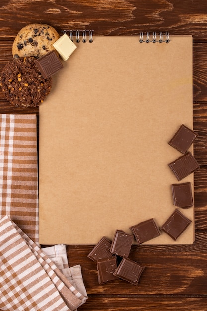 Photo gratuite vue de dessus du carnet de croquis avec des morceaux de chocolat noir et des biscuits à l'avoine sur fond de bois