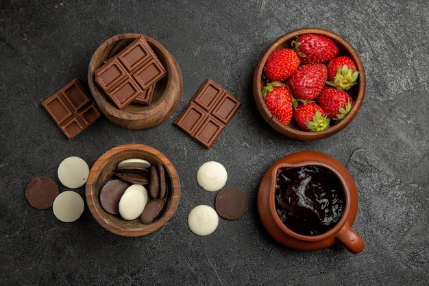 Vue de dessus du chocolat sur la table des bols bruns de fraises au chocolat et de la sauce au chocolat sur la surface sombre