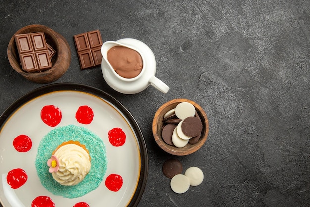 Vue de dessus du chocolat sur la table cupcake avec de la crème et des sauces à côté des bols de chocolat et de la crème au chocolat sur la table noire