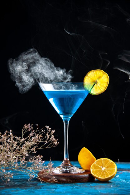 Vue de dessus du cocktail alchocol dans un gobelet en verre servi avec une tranche de citron et des branches de sapin sur une table bleue