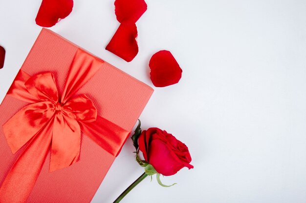 Vue de dessus du coffret rouge attaché avec un arc et une rose de couleur rouge et des pétales sur fond blanc