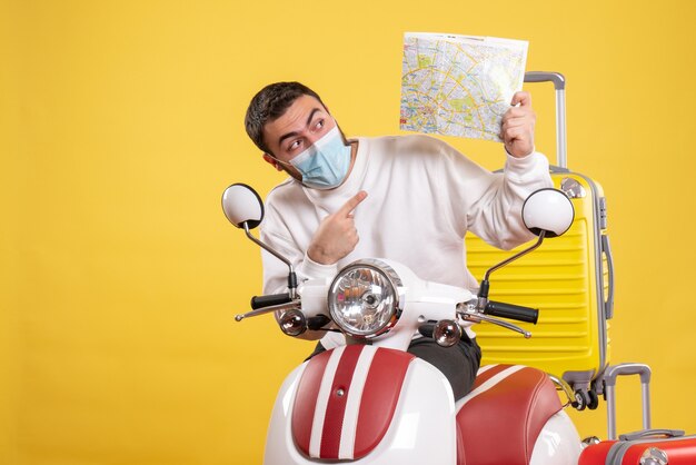 Vue de dessus du concept de voyage avec un gars curieux en masque médical debout près de la moto avec une valise jaune dessus et une carte de pointage