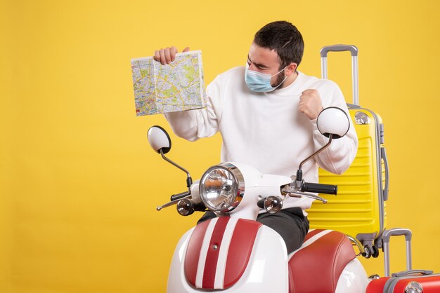 Vue de dessus du concept de voyage avec un gars fier en masque médical debout près de la moto avec une valise jaune dessus et tenant une carte