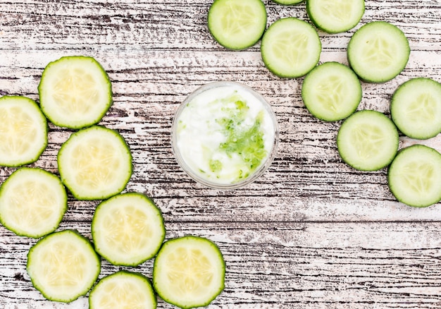 Photo gratuite vue de dessus du concombre en tranches avec du yaourt blanc dans un bol en verre sur l'horizontale en bois blanc