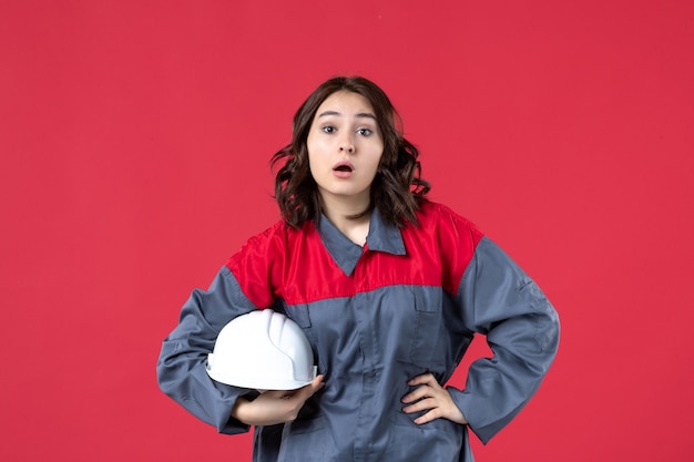 Vue de dessus du constructeur féminin surpris en uniforme et tenant un casque sur fond rouge isolé