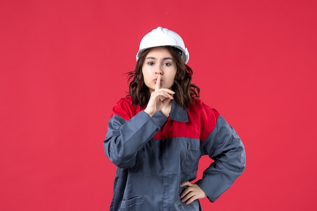 Vue de dessus du constructeur féminin en uniforme avec un casque et faisant un geste de silence sur fond rouge isolé