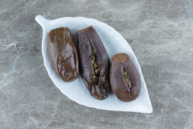 Vue de dessus du cornichon aux aubergines farcies sur une plaque blanche sur une table grise.