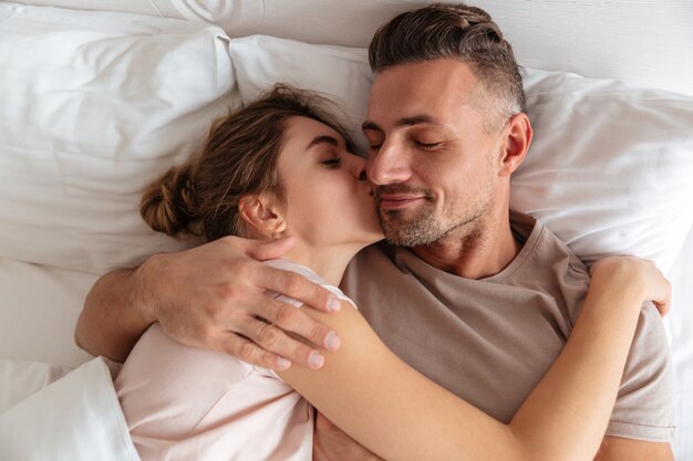 Vue de dessus du couple amoureux sensuel couché ensemble dans son lit à la maison pendant que la femme embrasse son petit ami