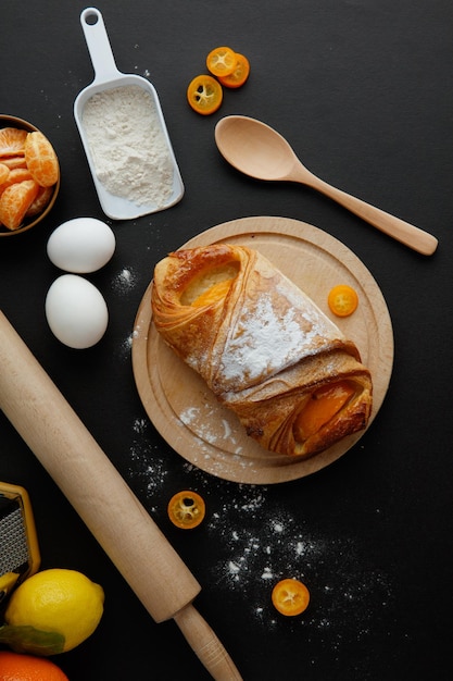 Vue de dessus du croissant sur dessous de plat avec de la farine d'oeuf kumquat citron mandarine cuillère et rouleau à pâtisserie sur fond noir