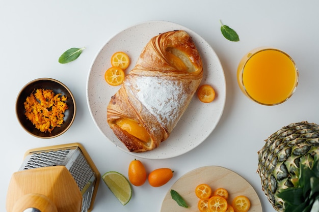 Vue de dessus du croissant avec des tranches de kumquat dans une assiette et du jus d'orange de zeste d'orange d'ananas avec râpe sur fond blanc