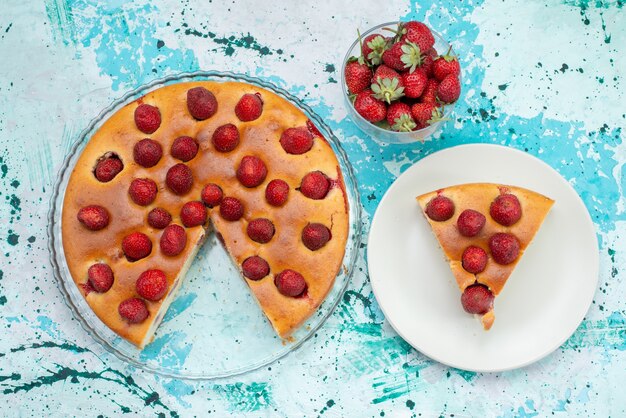 Vue de dessus du délicieux gâteau aux fraises en tranches et délicieux gâteau entier avec des fraises rouges fraîches sur un bureau bleu vif, gâteau aux baies