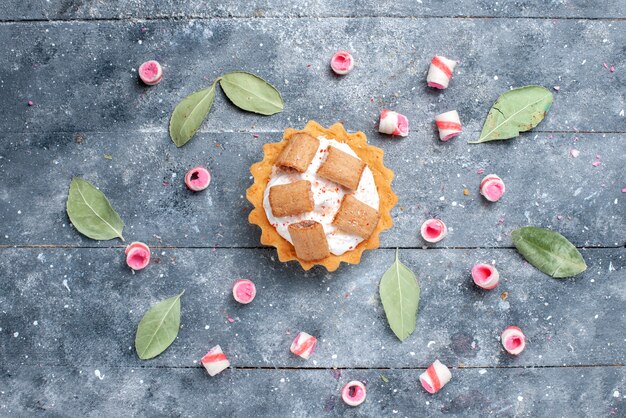 Vue de dessus du délicieux gâteau crémeux avec des biscuits avec des bonbons tranchés sur gris, gâteau sucré sucre cuit