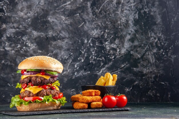 Vue de dessus du délicieux sandwich sur un plateau de couleur sombre et des pépites de poulet frites de tomates sur une surface noire