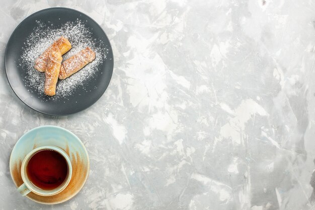 Vue de dessus du délicieux sucre de bagels sucré en poudre avec une tasse de thé sur une surface blanche